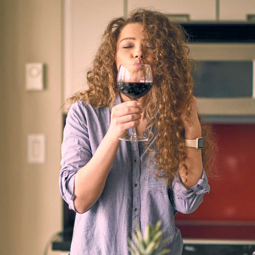 a woman smelling and tasting red wine